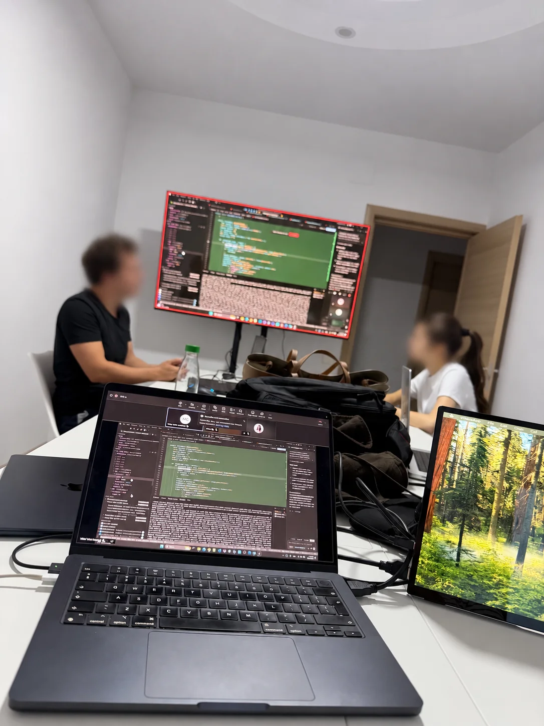 Coworking at the office with laptops and a large screen showing code